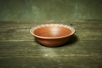 Handmade rustic clay bowl with hand-engraved rim on wooden surface, artisan homeware