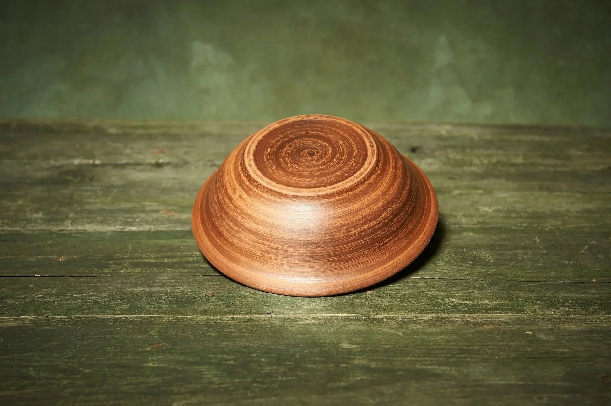 Handmade rustic clay bowl with woodgrain pattern on green wooden surface