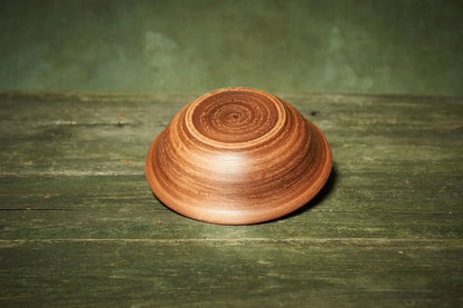 Handmade rustic clay bowl with woodgrain pattern on green wooden surface