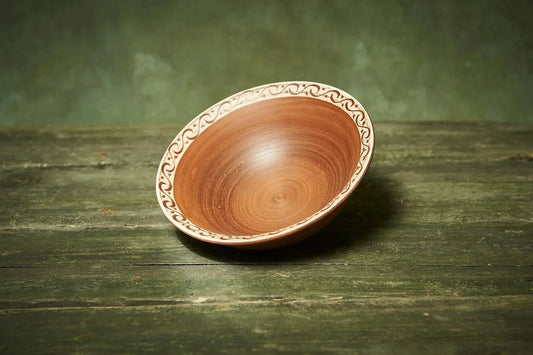 Handmade clay bowl with hand-engraved rim on rustic wooden surface, artisan homeware