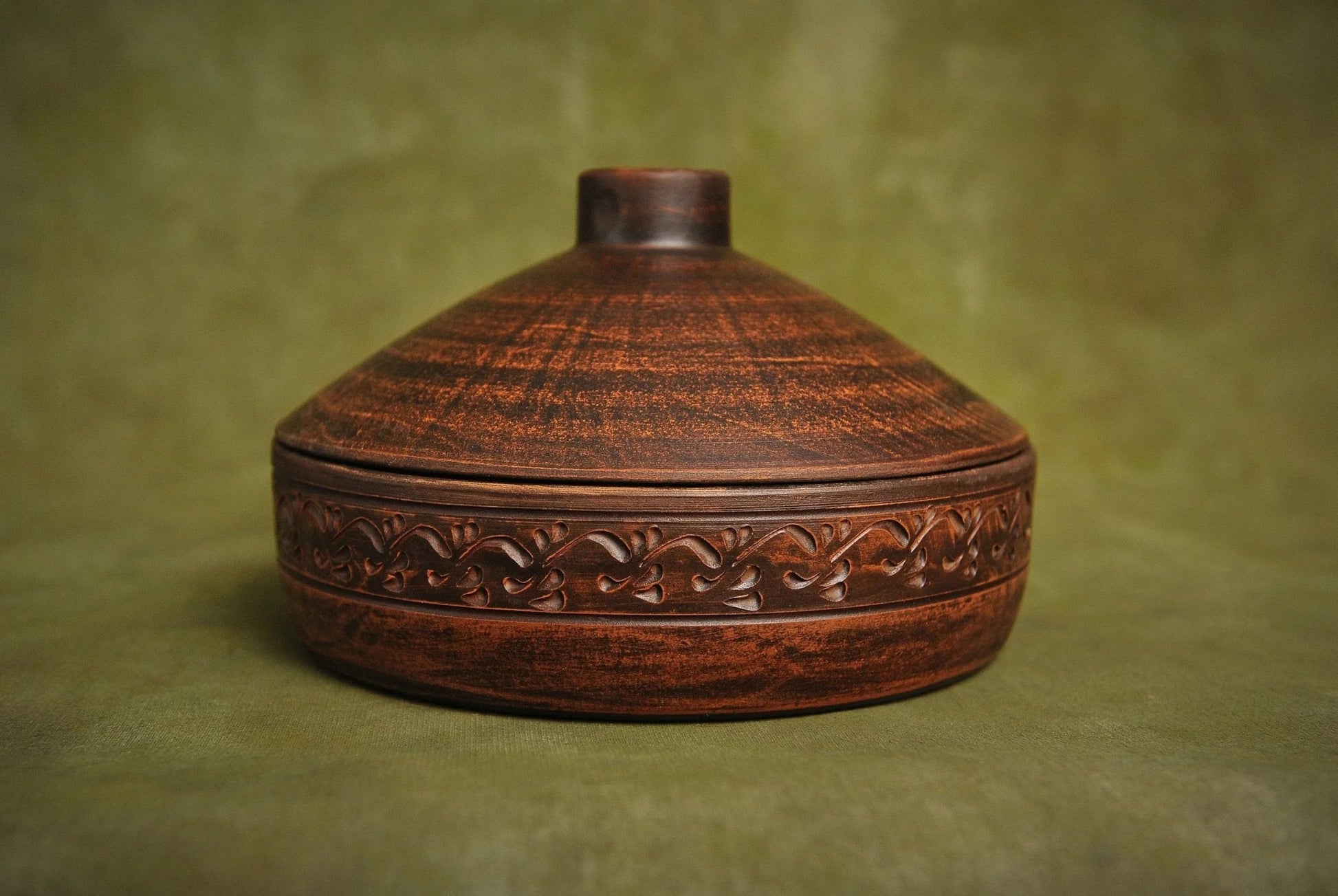Handmade clay cooking pot with ornate carved design, artisan ceramic cookware on green background
