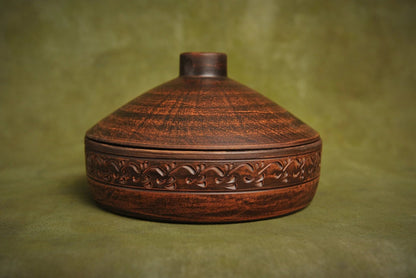 Handmade clay cooking pot with ornate carved design, artisan ceramic cookware on green background
