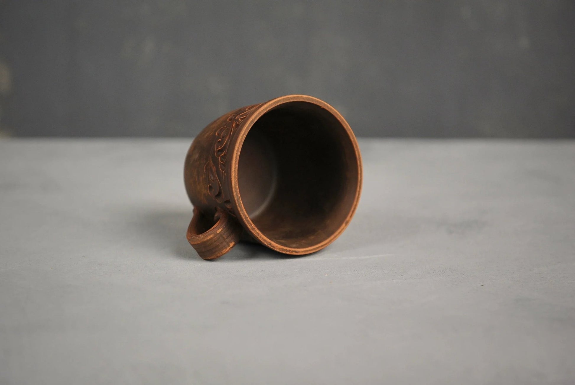 Handmade clay cup with carved ethnic patterns on a gray background, artisan ceramic tumbler