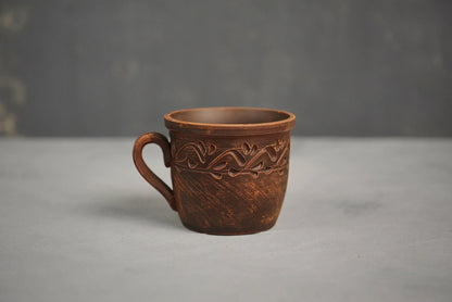 Handmade red clay cup with ethnic carved design on gray background, artisan pottery home decor