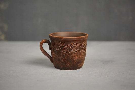 Handmade red clay cup with ethnic carved design on gray background, artisan pottery home decor