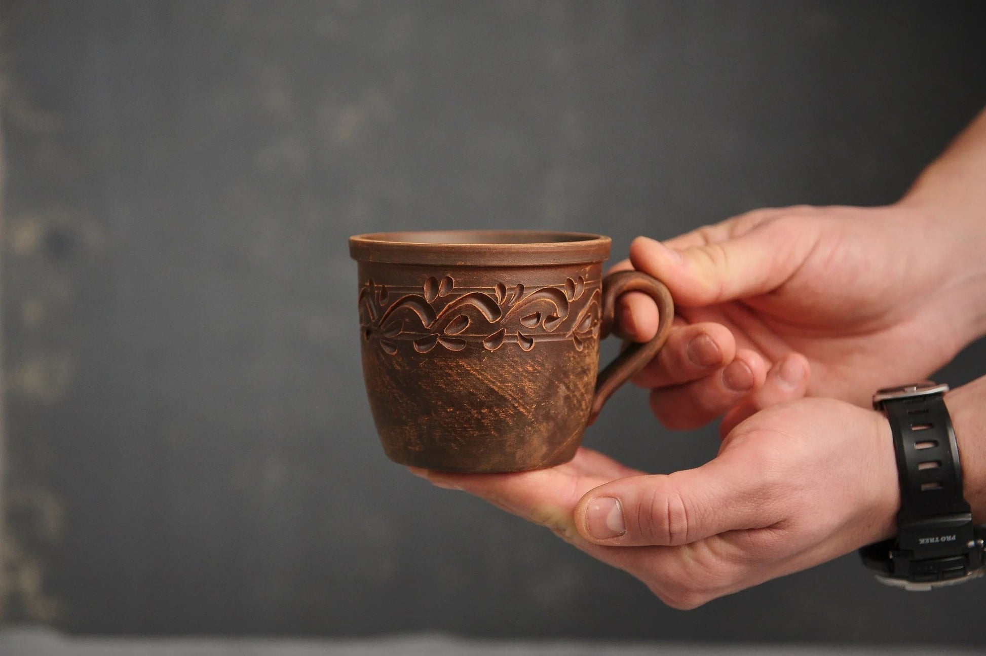 Hand holding a handmade clay cup with ethnic carved pattern, organic ceramic homeware