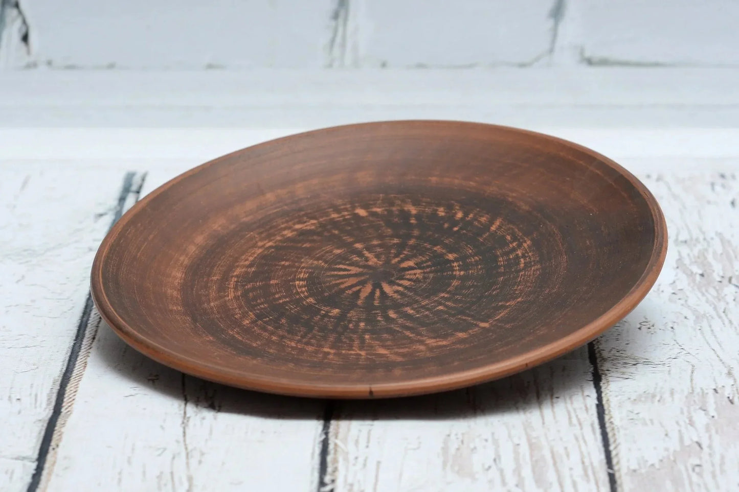 Handmade brown clay dinner plate with rustic finish on white wood background
