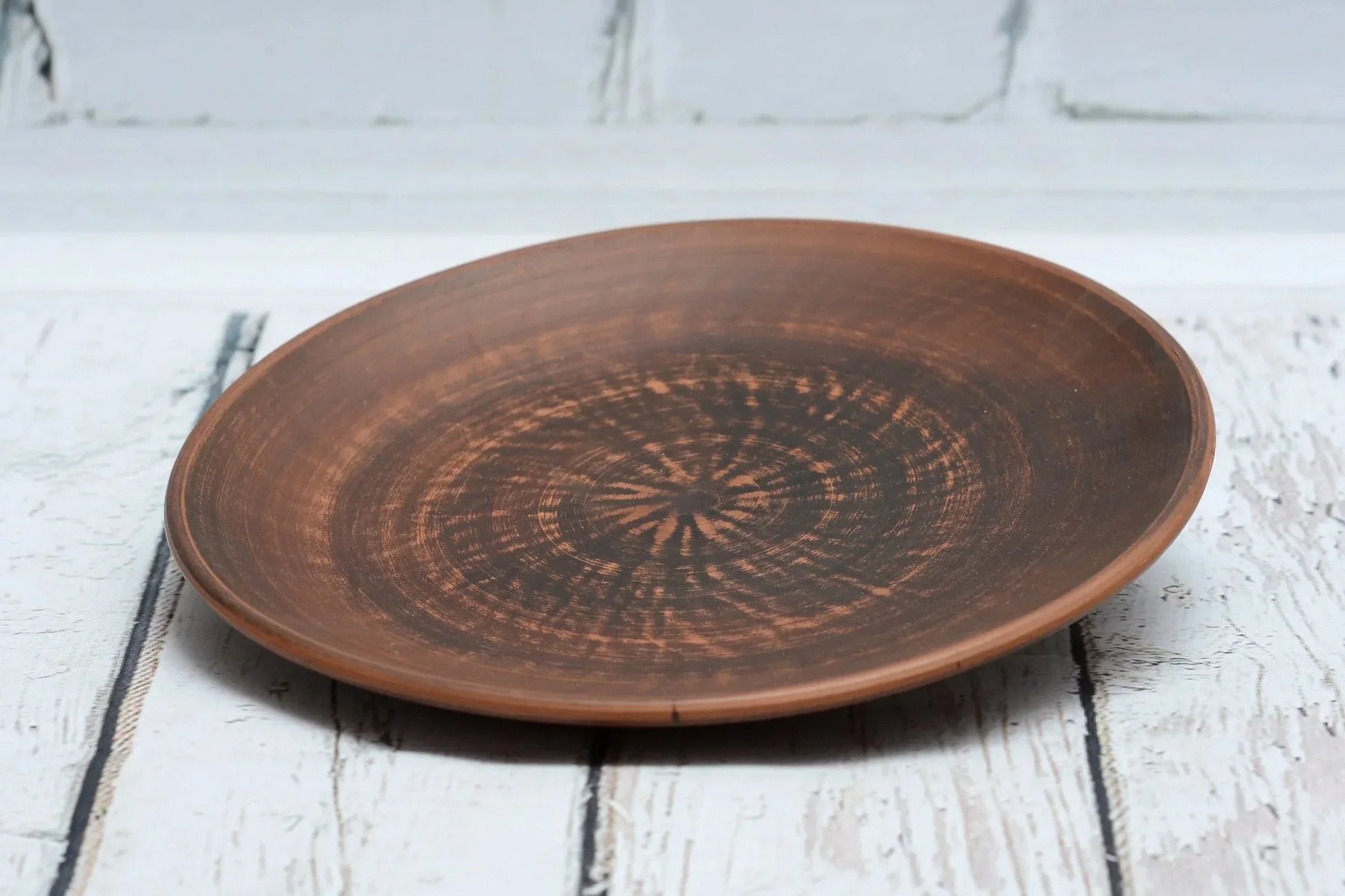 Handmade brown clay dinner plate with rustic finish on white wood background