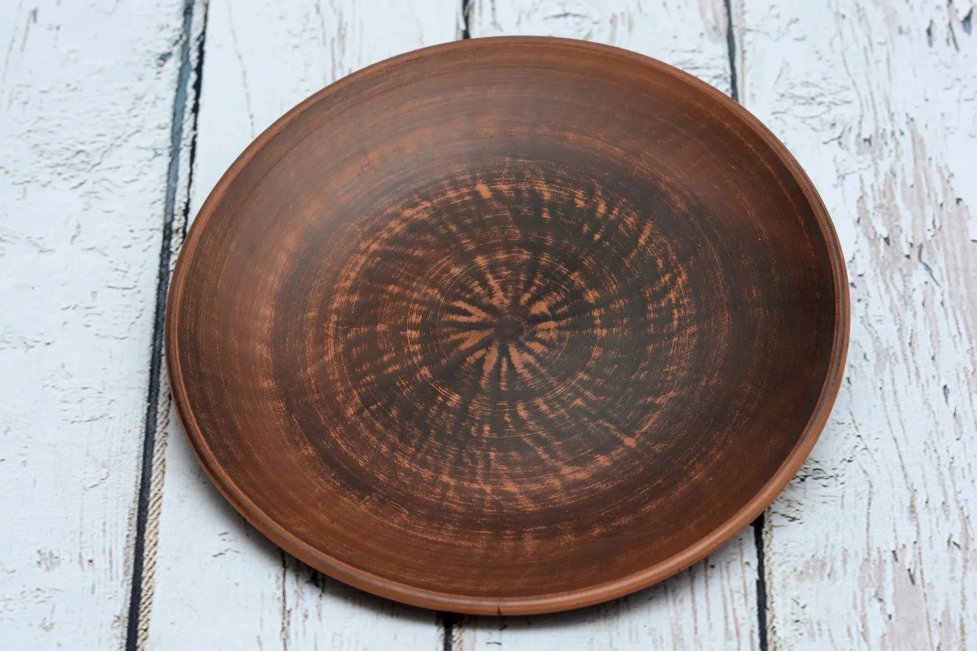 Handmade clay dinner plate with rustic finish on white wooden surface, artisan pottery homeware