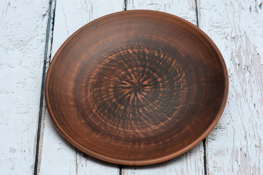 Handmade clay dinner plate with rustic finish on white wooden surface, artisan pottery homeware