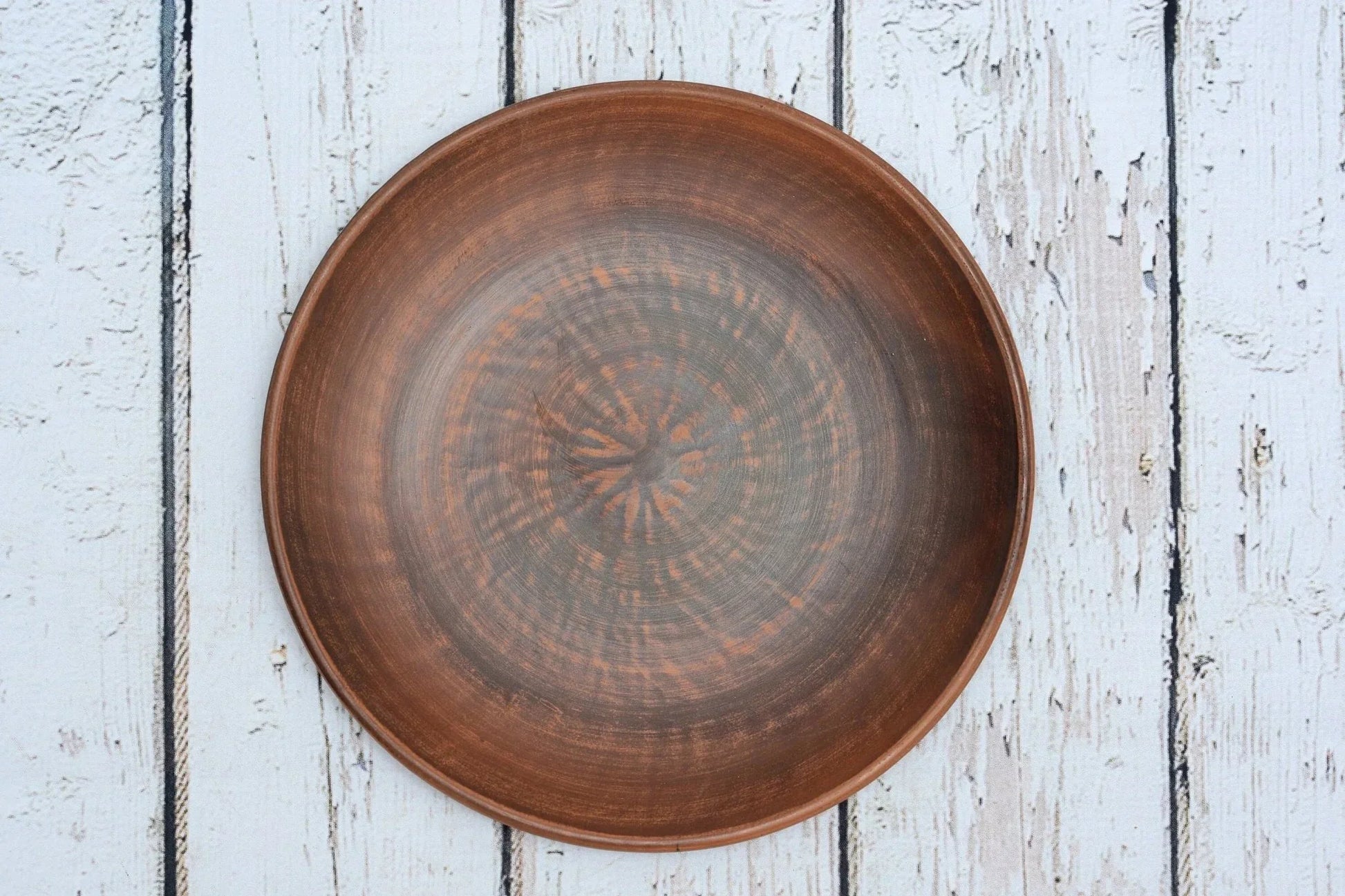 Handmade clay dinner plate with rustic brown design on white wooden background