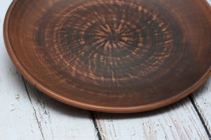Handmade clay dinner plate with rustic brown pattern on wood background, artisan pottery homeware