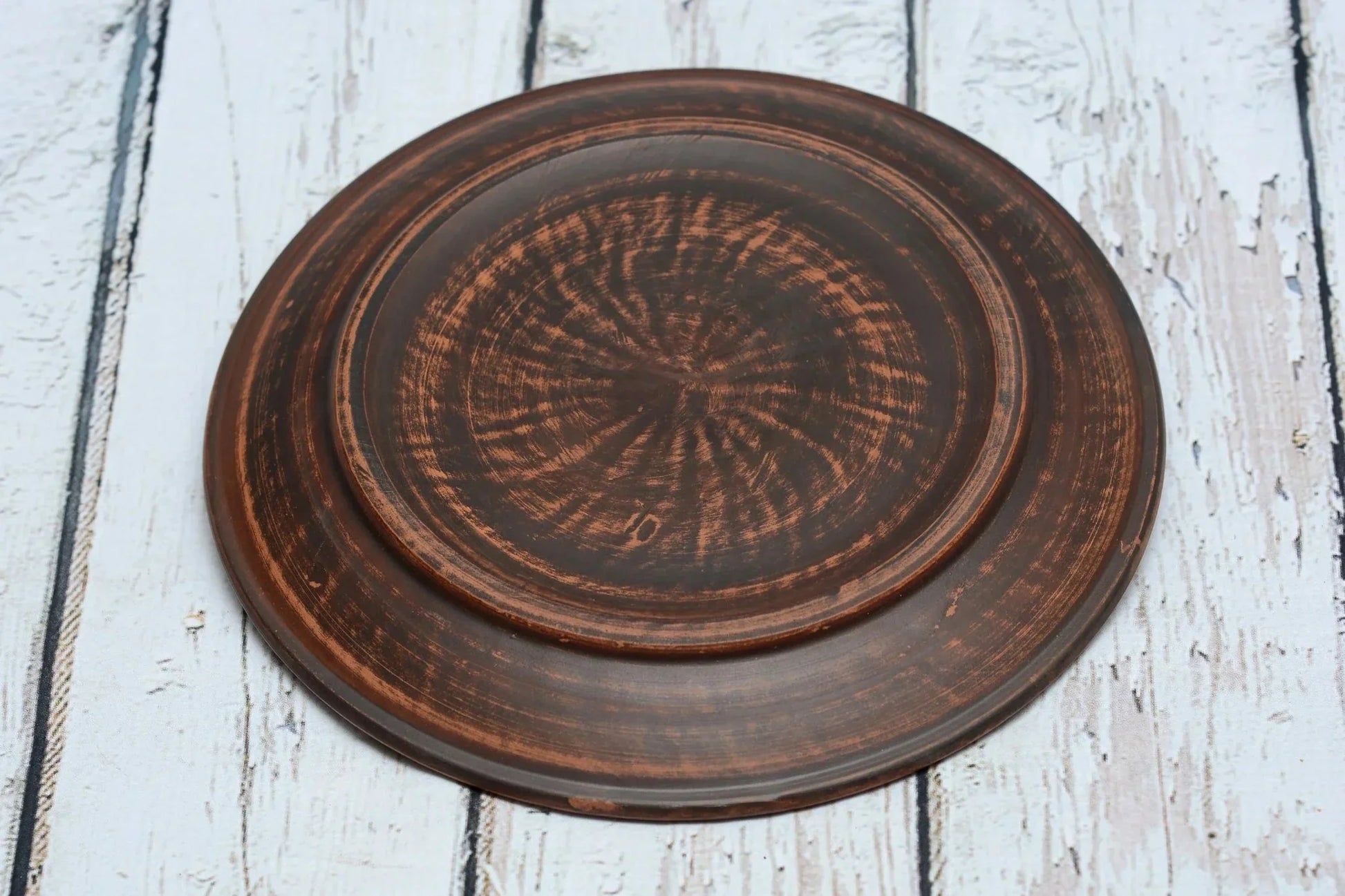 Handmade round clay dinner plate with rustic brown finish on white wood background