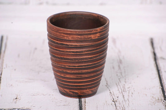 Handmade clay tumbler with ribbed texture, artisan pottery cup on rustic white wood.