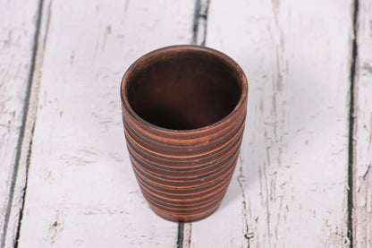 Handmade clay tumbler with grooved texture on rustic wood background, eco-friendly pottery cup
