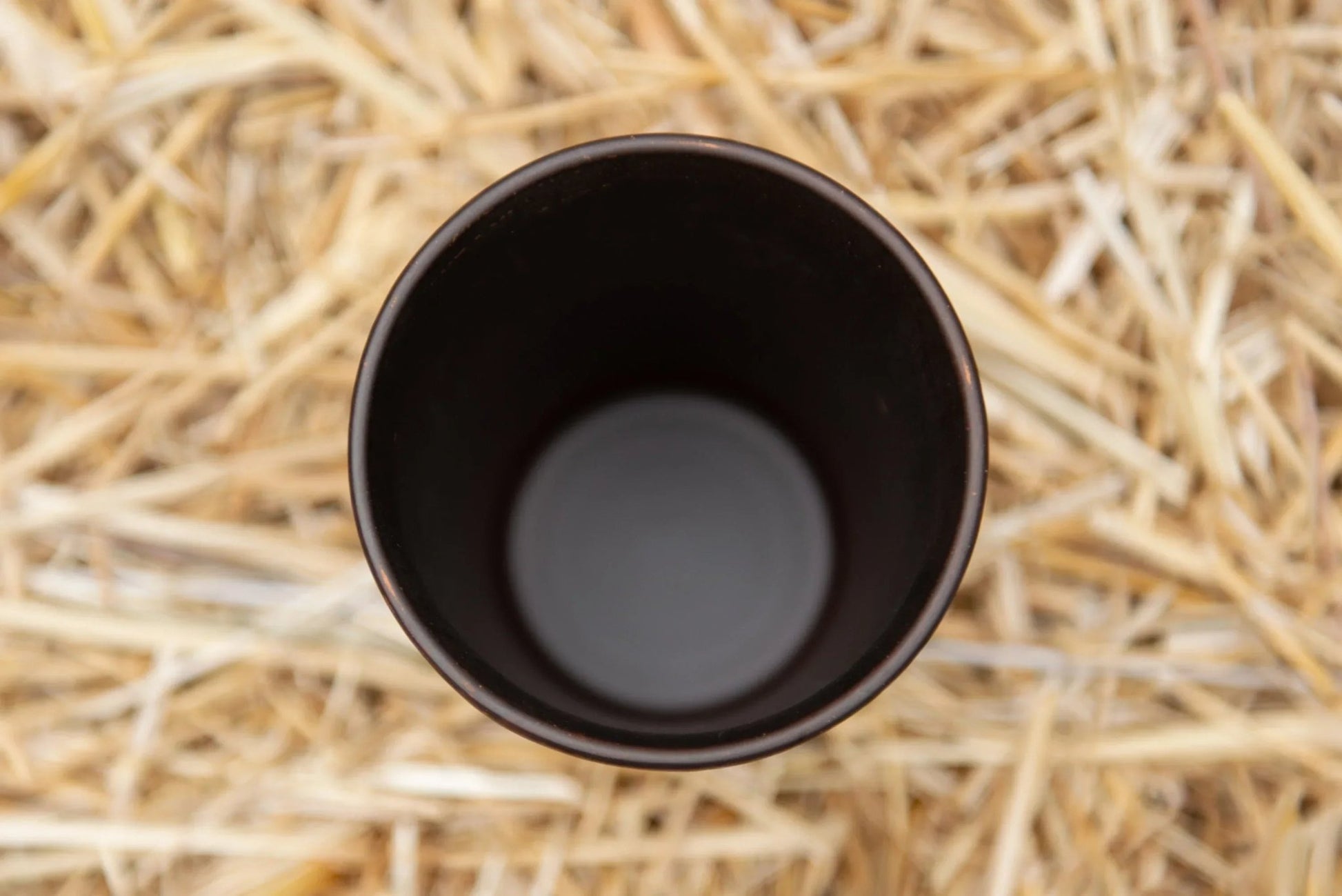 Handmade clay drinking glass with dark interior on straw background, artisan eco homeware