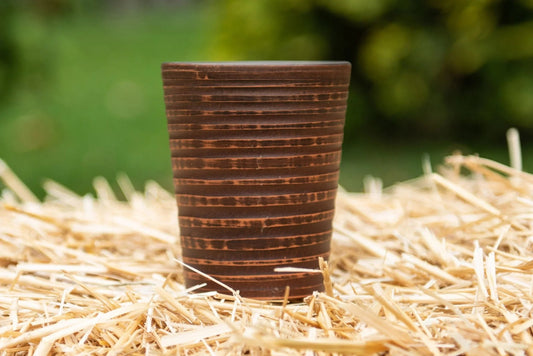 Handmade clay drinking glass with ribbed texture on straw, artisan eco pottery tumbler