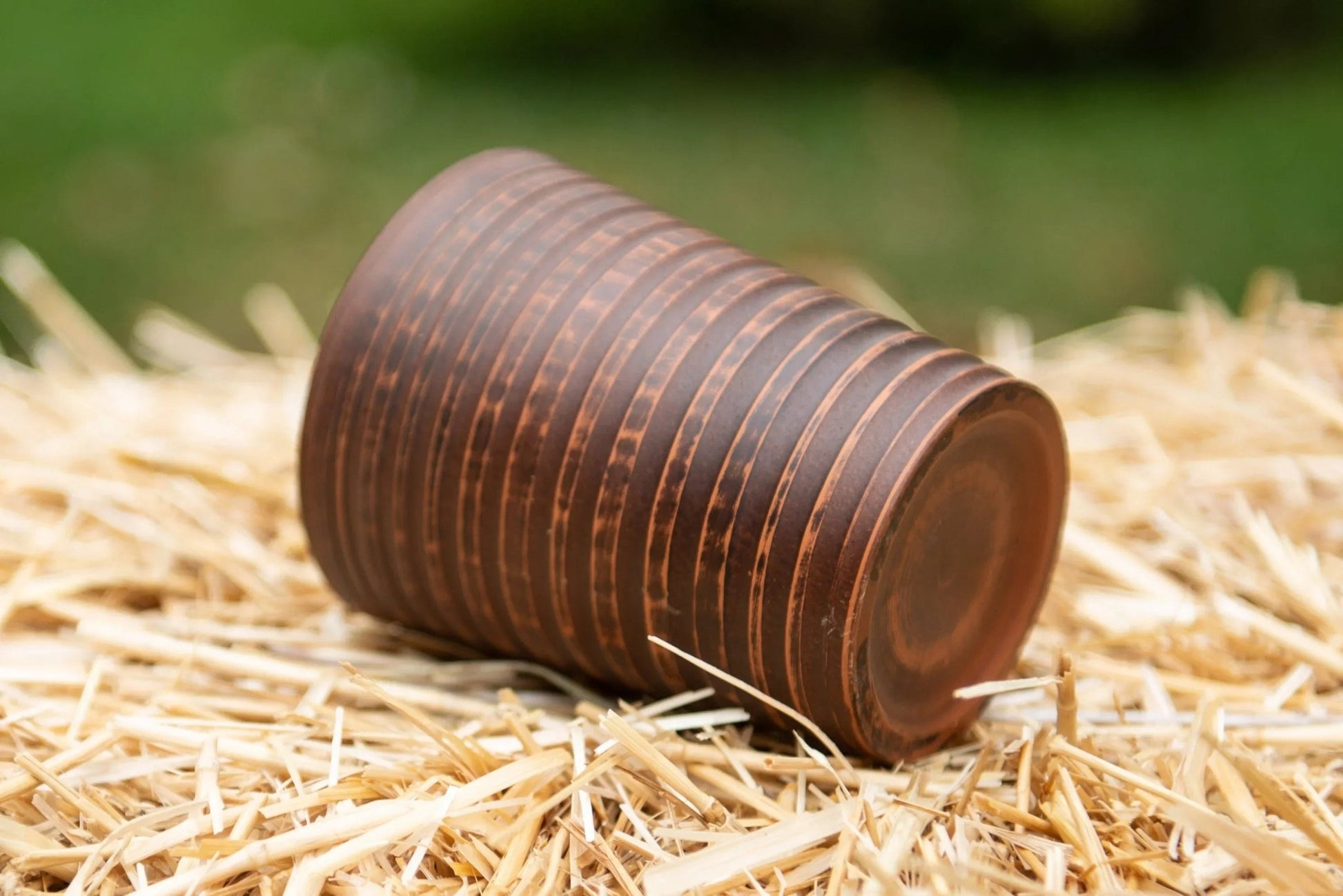 Handmade clay tumbler with textured brown stripes on straw, eco-friendly pottery cup