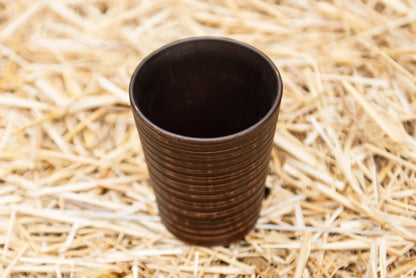 Handmade clay drinking glass with ribbed texture on straw background, artisan pottery cup