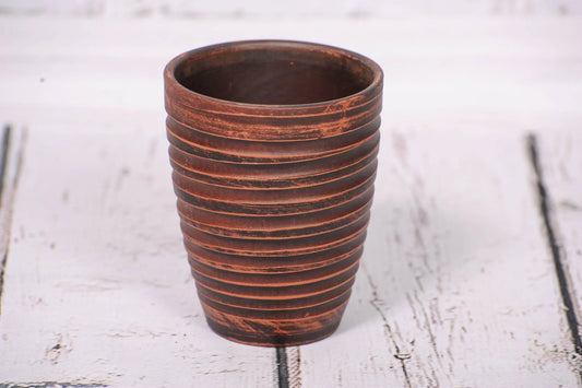 Handmade clay tumbler with textured stripes on rustic white wood, artisan pottery cup