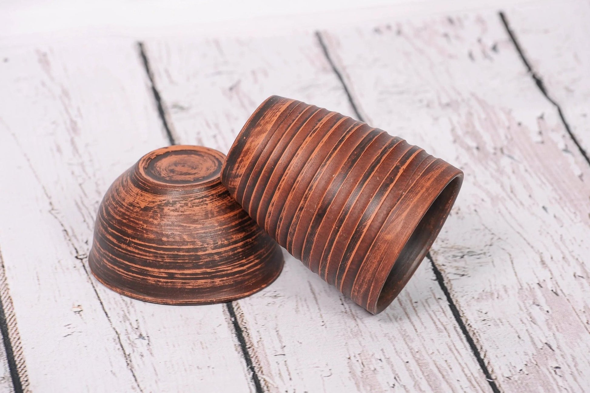 Handmade clay drinking glasses with rustic brown finish on a white wooden surface