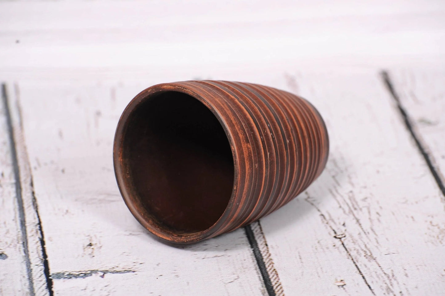 Handmade clay tumbler with ribbed texture on white wooden surface, artisan pottery cup