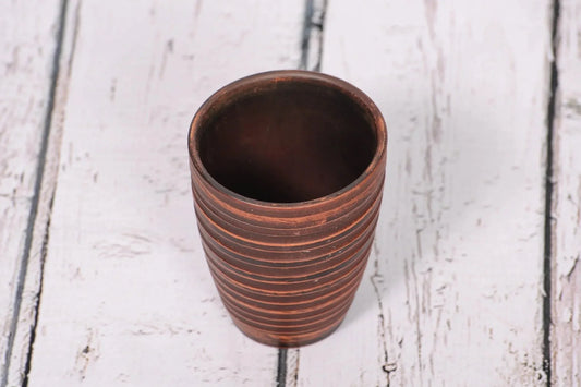 Handmade clay pottery tumbler with textured lines on rustic wooden surface