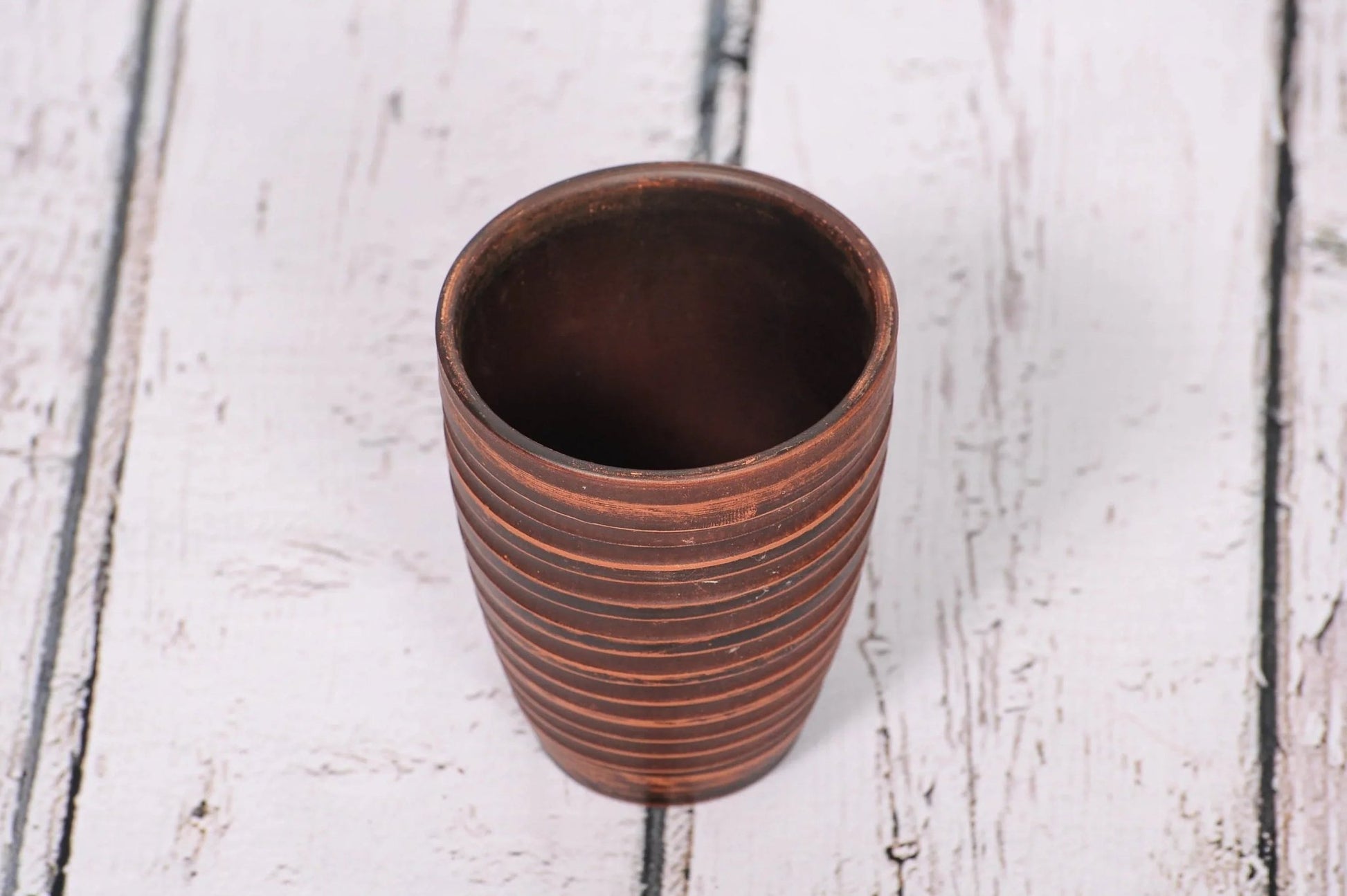 Handmade clay pottery tumbler with textured lines on rustic wooden surface