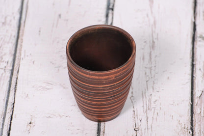 Handmade clay pottery tumbler with textured lines on rustic wooden surface