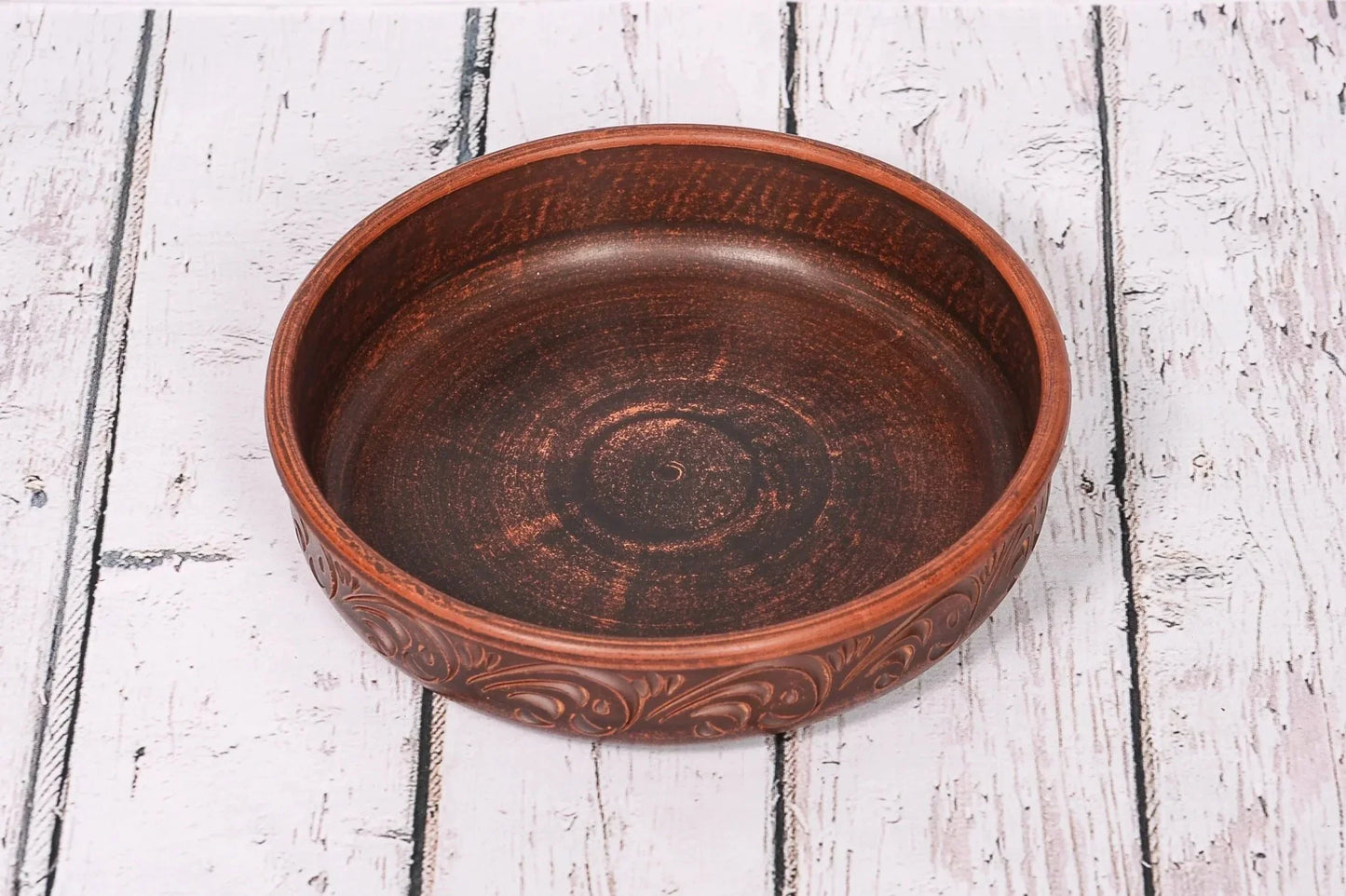 Handmade clay pancake maker plate with carved design on rustic wood background