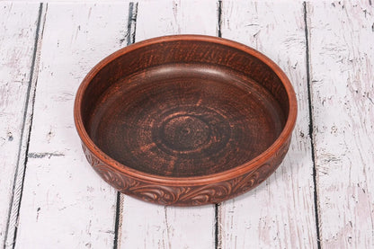 Handmade clay pancake maker plate with carved design on rustic wood background