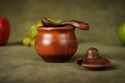 Handmade clay salt bowl with spoon and lid, artisan ceramic kitchenware on rustic background