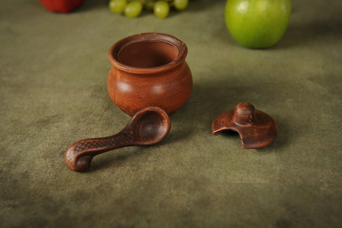 Handmade clay salt bowl with spoon and lid on green background, artisan ceramic homeware