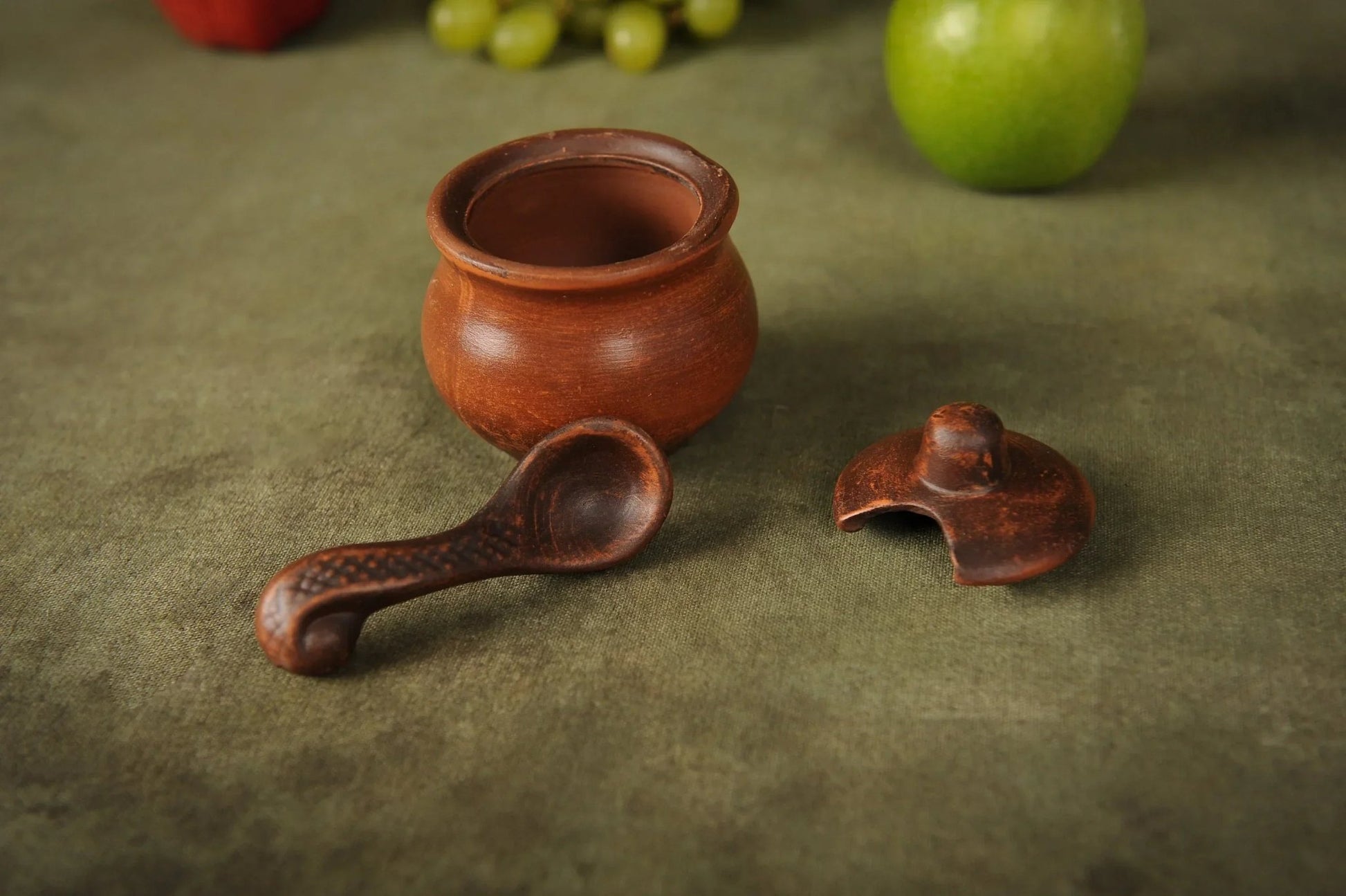 Handmade clay salt bowl with spoon and lid on green background, artisan ceramic homeware