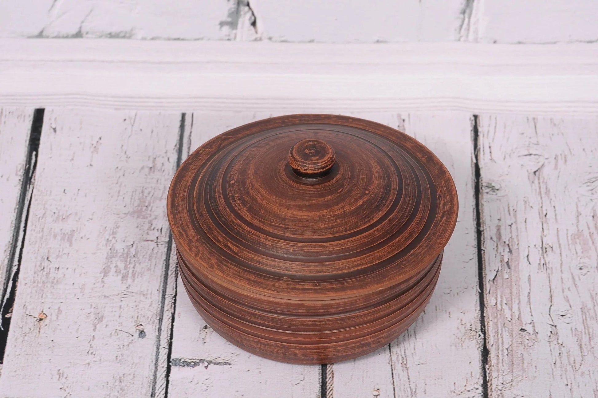 Handmade ceramic clay cooking pot with lid, rustic brown, on white wooden surface