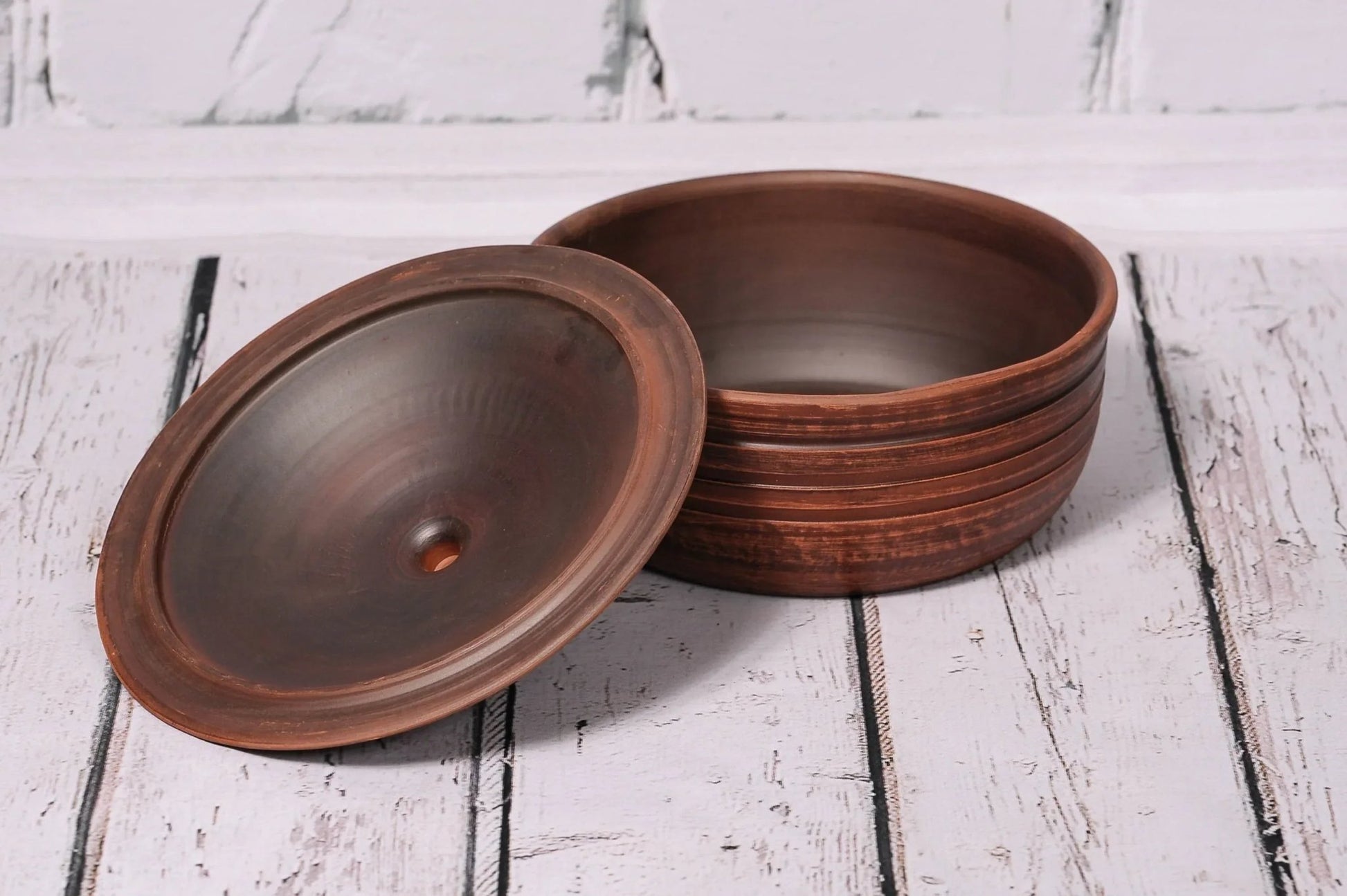 Handmade clay ceramic baking dish with lid on rustic wooden table, artisan kitchenware