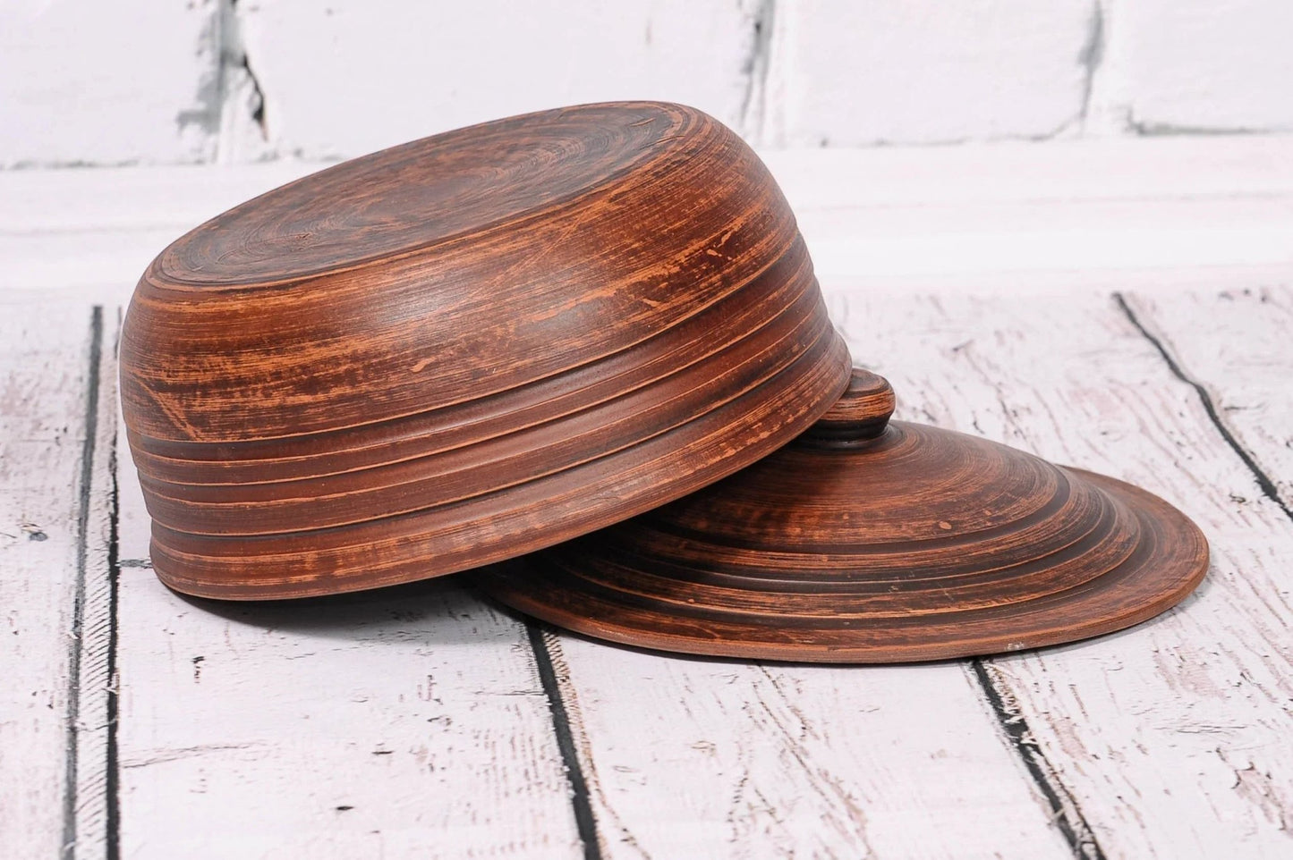 Handmade brown clay baking dish and lid with rustic texture on white wood background