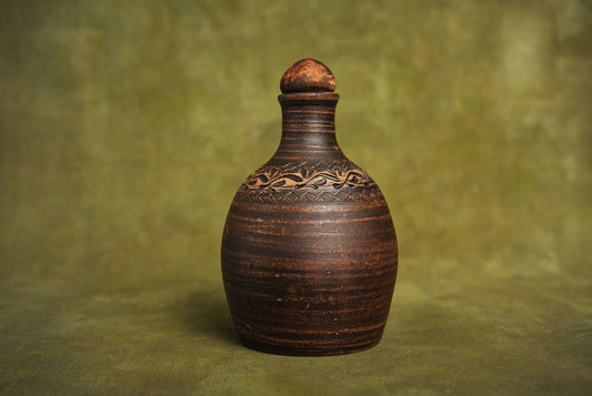 Handmade red clay bottle with carved decorative pattern, rustic homeware on green background