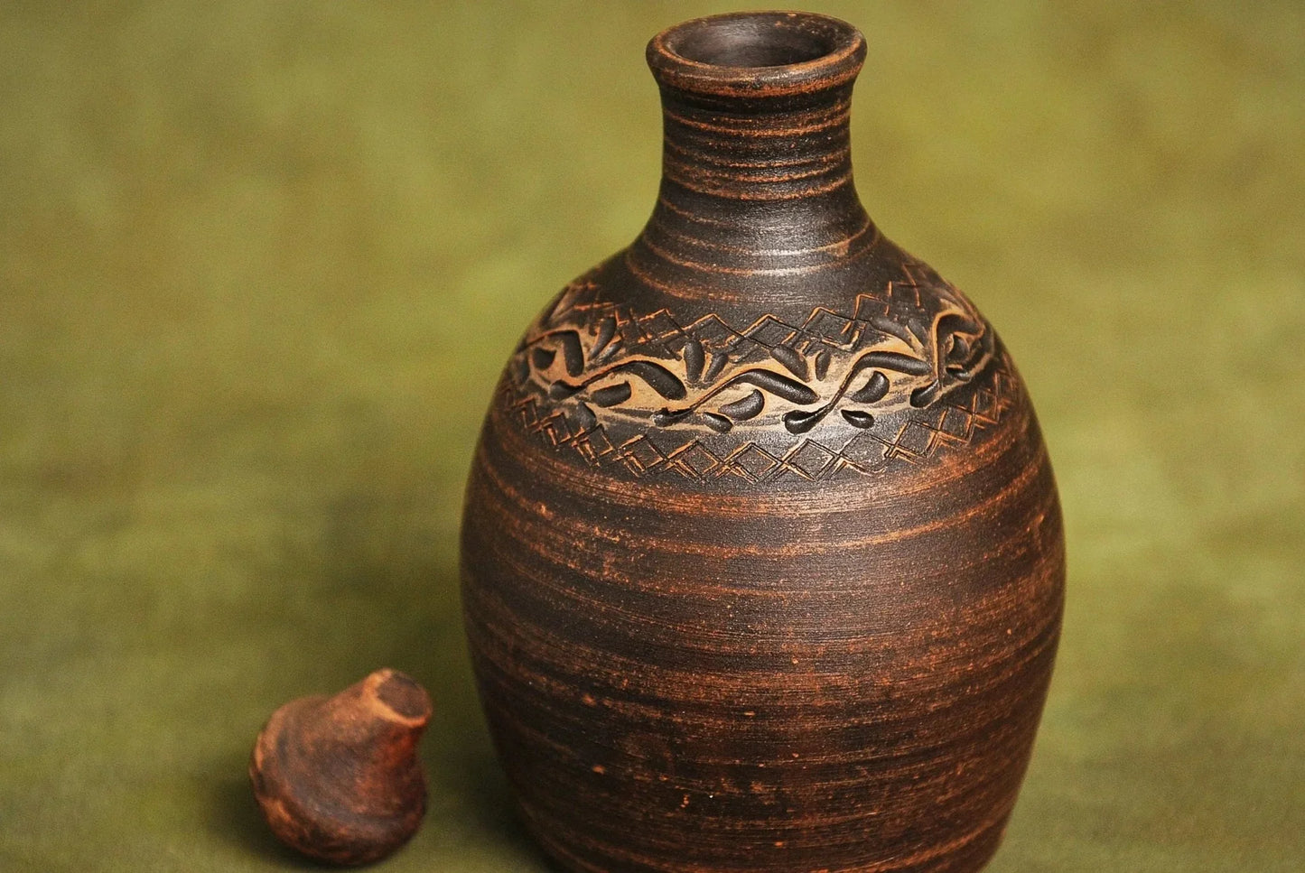 Handmade red clay bottle vessel with carved pattern on green background, artisan home décor