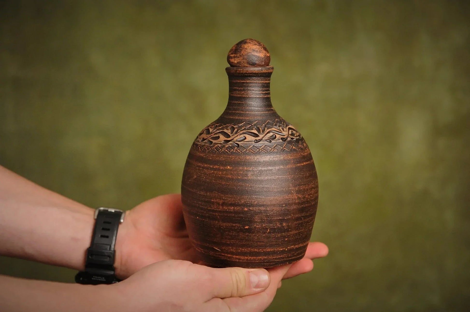 Hand holding a handmade red clay bottle with carved pattern, artisan homeware from clayproductsshop