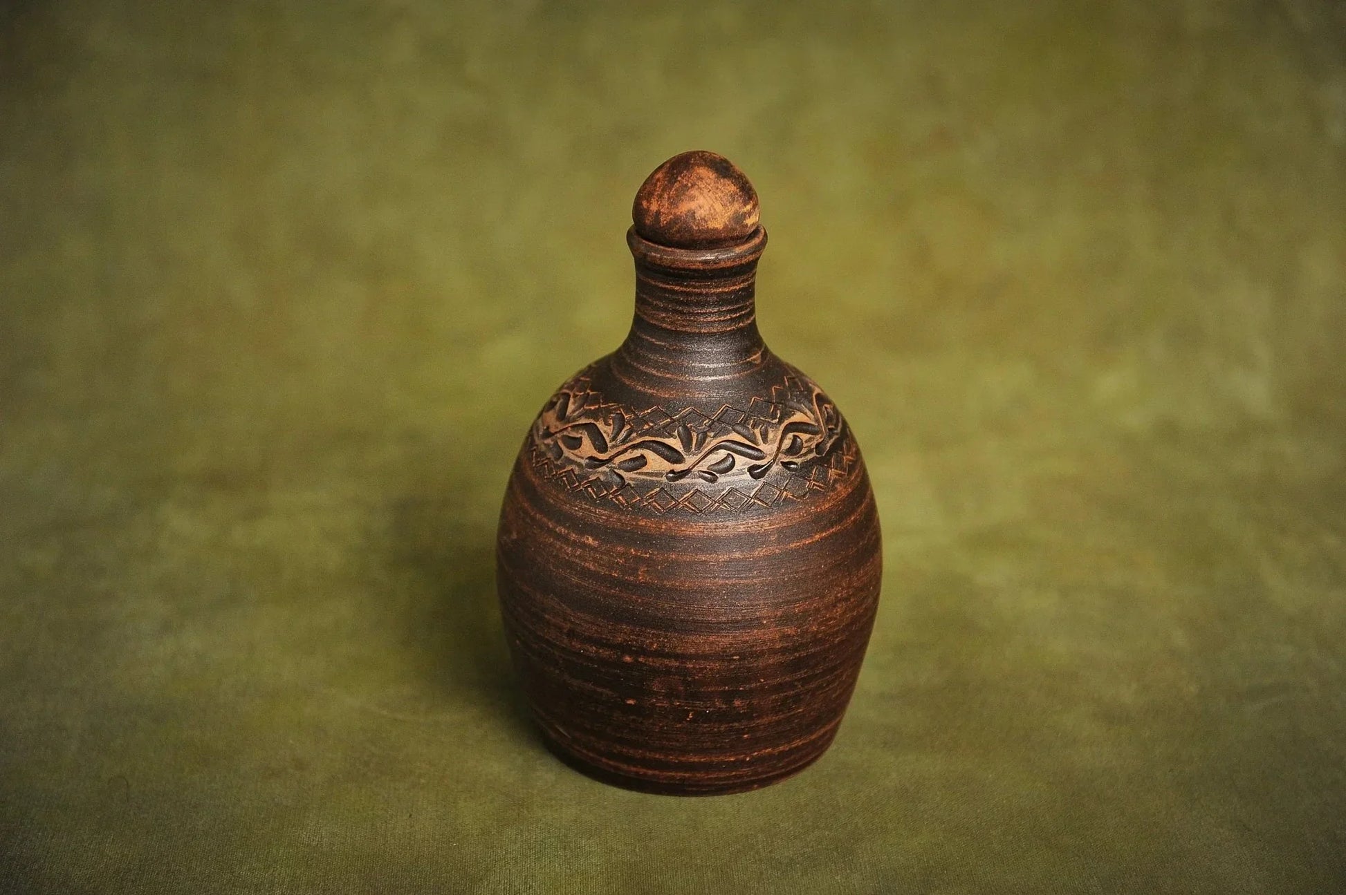 Handmade red clay bottle with ornate carved design on green background