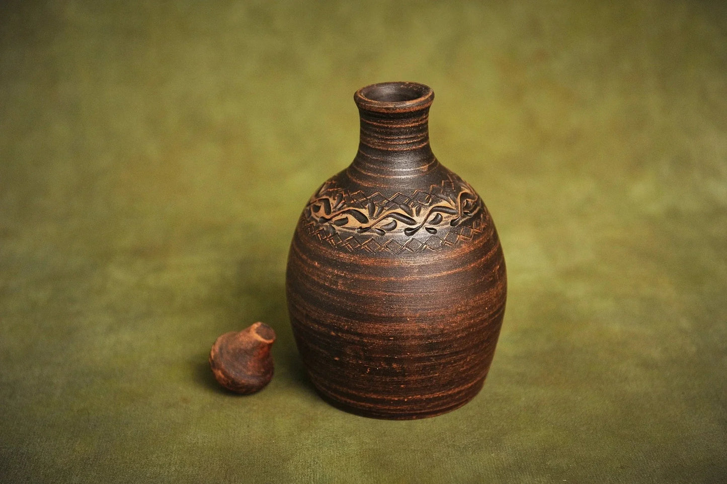 Handmade red clay bottle jug with carved pattern on green background, artisan homeware