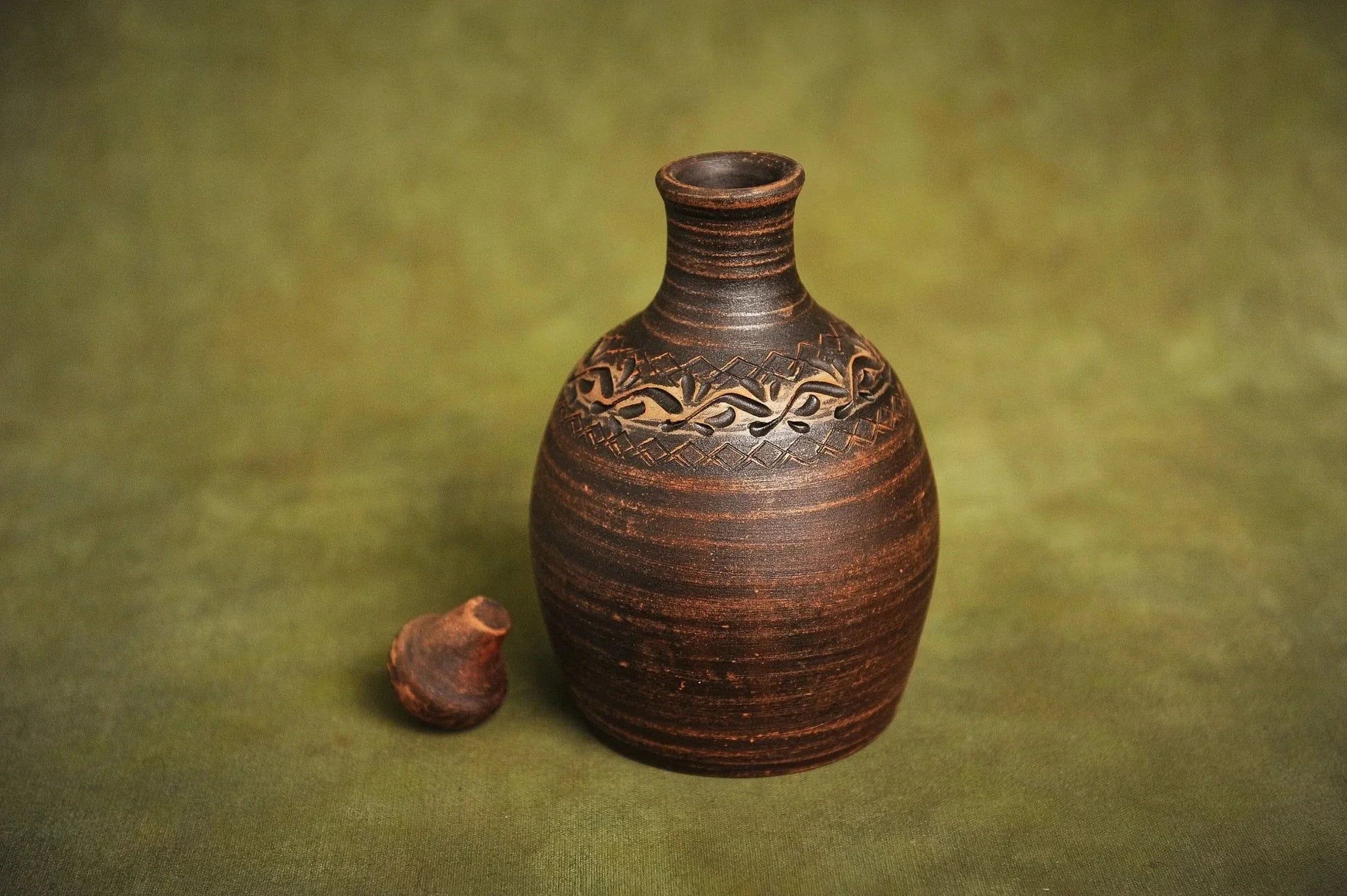 Handmade red clay bottle jug with carved pattern on green background, artisan homeware