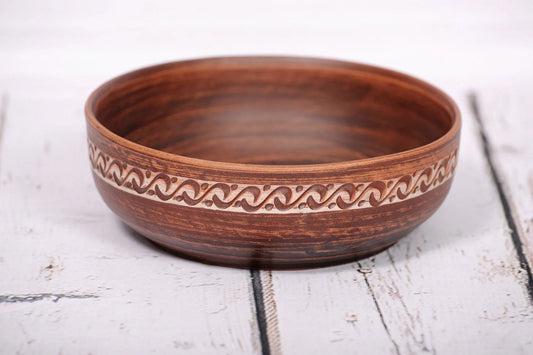 Handmade red clay bowl with rustic pattern, artisan ceramic dish on white wooden surface