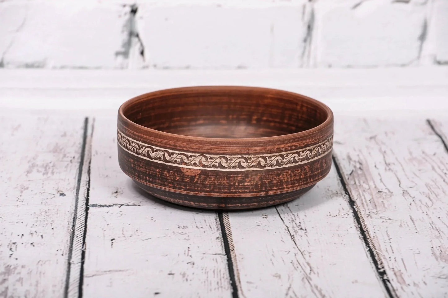 Handmade red clay bowl with etched design, rustic ceramic kitchenware on wooden surface