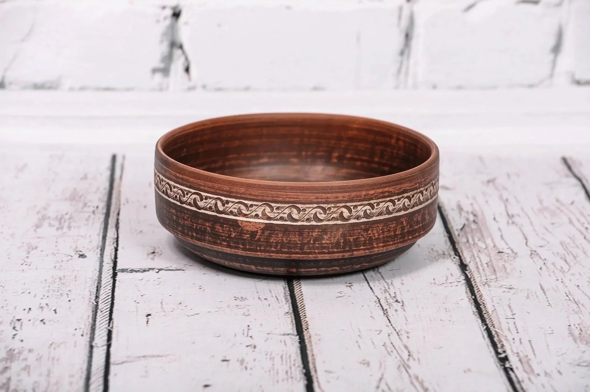 Handmade red clay bowl with etched design, rustic ceramic kitchenware on wooden surface