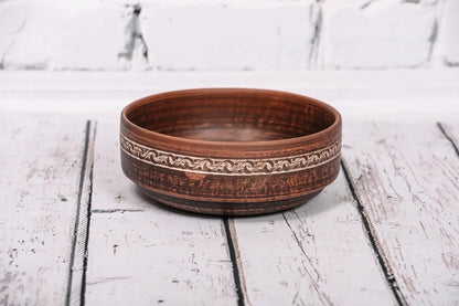 Handmade red clay bowl with etched design, rustic ceramic kitchenware on wooden surface