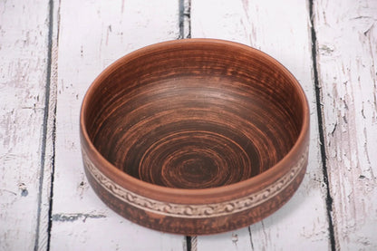 Handmade red clay bowl with rustic pattern, artisan ceramic homeware on white wooden table