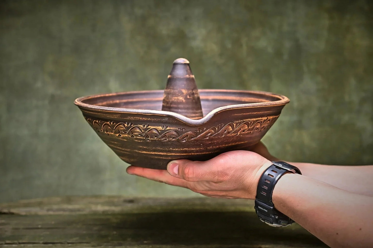 Handmade unglazed ceramic chicken roaster plate with floral carvings, held by hand