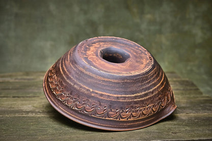 Handmade unglazed ceramic chicken roaster with carved patterns on rustic wooden surface